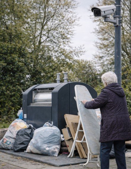 Camera op paal gericht op ondergrondse afvalcontainer met grofvuil en afvalzakken ernaast